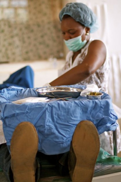 A health worker in a hair net, face mask, and gloves attends to a patient who lays prone on a table. Only the soles of his shoes are visible.