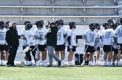 Coach Pete Milliman stands in front of lacrosse players on Homewood Field