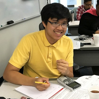 Student in yellow polo shirt poses for photo while working with notebook, calculator