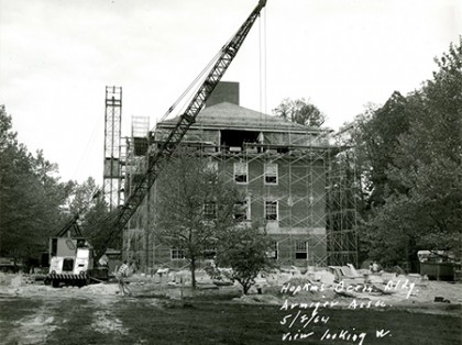 Black and white image of crane towering over brick campus building