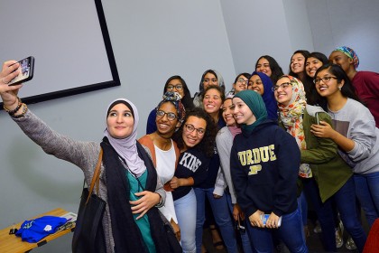 Linda Sarsour holds phone and takes selfie with group of about 15 students