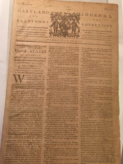 A yellowed parchment newspaper shows a published version of the Declaration of Independence