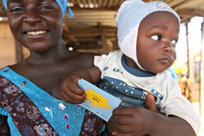 A woman holds a baby who is holding a card labeled 