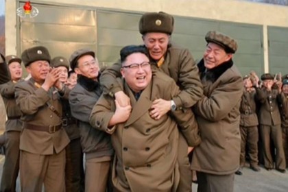 An older man in a military coat jumps on the back of a smiling Kim Jong-Un