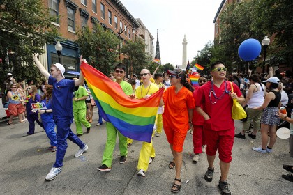A group in blue, green, yellow, orange, and red scrubs hold the pride flag
