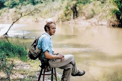 Reds Wolman sits on a stool beside a river