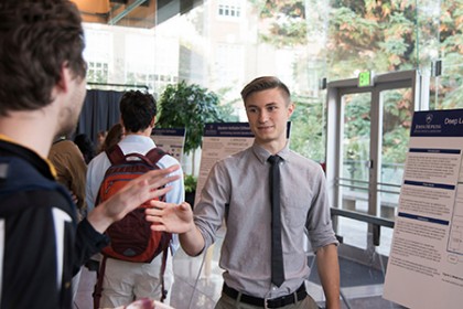 A young man in a tie gestures to people who are listening to his presentation