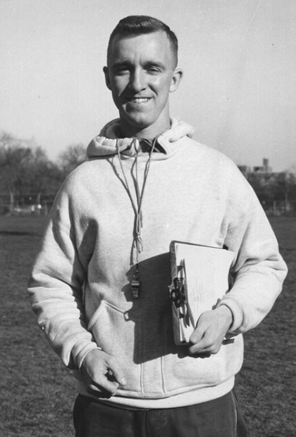 Black and white photo of Bob Scott in hooded sweatshirt holding a clipboard
