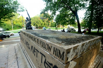 An empty statue plinth is vandalized with graffiti