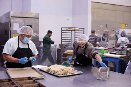 Wearing masks and hair nets, men work in an industrial kitchen operated by Homeboy Industries
