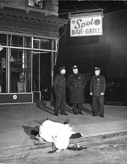 A group of police officers stand beside a dead body at a diner