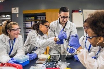 Three students watch as a fourth pipes liquid into a test tube held by a graduate student volunteer