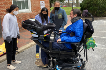 A man in a wheelchair speaks to three people, standing around him