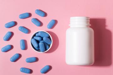 Unlabeled bottle of blue pills on a pink background