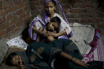 A mother holds a little boy while another woman sleeps on her side