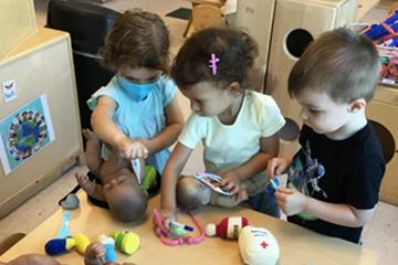 Three toddlers play pretend doctor with dolls and plastic medical equipment
