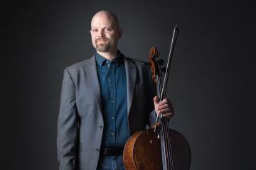 Alum Joel Dallow stands with a cello