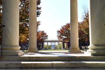 A campus scene featuring four marble columns and marble steps, with fall foliage in the background