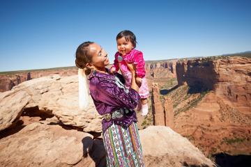 A woman holds a smiling child in a rocky desert setting
