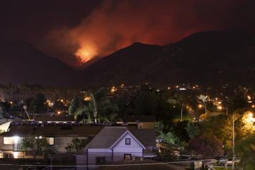 A wildfire approaches over the crest of a mountain ridge with a neighborhood of houses in the valley below