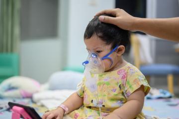 A toddler receives treatment in the hospital for RSV, wearing a mask to help them breathe.