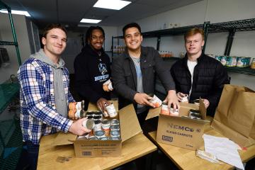 Four young men pose for a photo while unpacking boxes of canned carrots