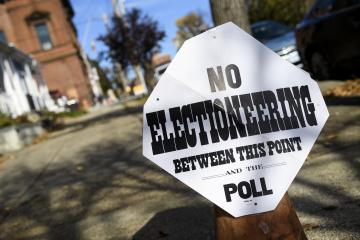 A white sign with black text posted on a city street says "no electioneering between this point and the poll"