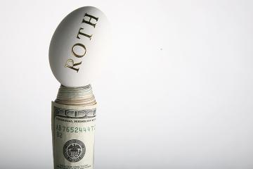 An egg with the word Roth on it sits atop rolled-up money