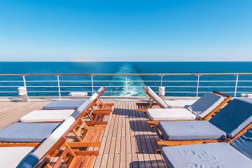 Empty lounge cchairs on a ship's deck overlooking the sea
