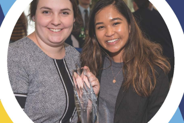 Two smiling women in professional dress hold a glass trophy