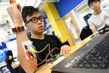 A student with red, blue, yellow, and green wires attached to a sensor on his forearm