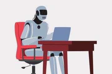 A robot sits at a desk in a red chair with a laptop