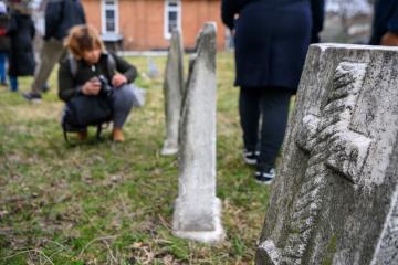 A student kneels down next to a grave stone at Mount Auburn Cemetery in Baltimore