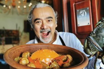 Restaurateur Dharshan Munidasa smiles while holding a bowl of crabs 