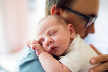 A father holds on a sleeping infant on his shoulder