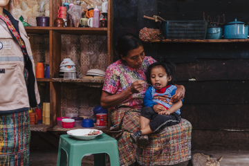 An older woman spoonfeeds her granddaughter black beans