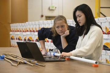 Two Johns Hopkins students look at a shared laptop on a long wooden work table at Blind Industries and Services of Maryland