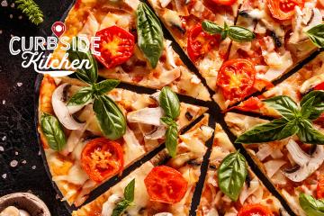 Closeup of a pizza topped with sliced tomatoes, mushrooms, and basil.