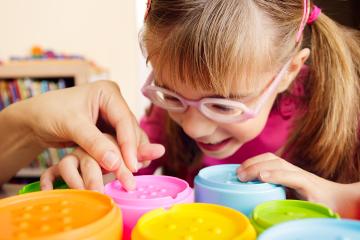 Young girl with poor vision touching tactile toy cups with her occupational therapist