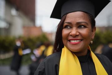A mature woman wears an academic robe and mortarboard at her graduation ceremony