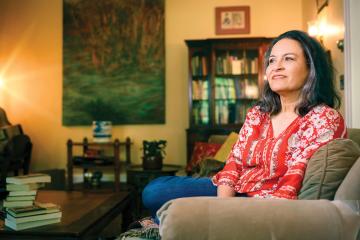 Sujata Massey sits in her living room next to a stack of books