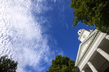 Blue skies with bright white clouds, looking up toward the Gilman Hall clock tower 