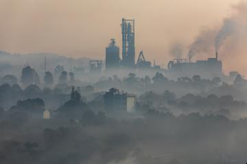 Smoke drifts from the smokestacks of an industrial plant on a foggy morning