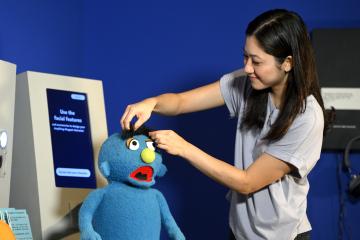 An intern at the MCHC's Jim Henson exhibition puts eyebrows on a puppet.