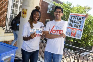 Two people hold up stickers and a poster that reads 