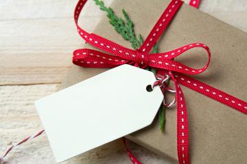 A festively wrapped package has a red ribbon, a sprig of greenery, and a blank gift tag