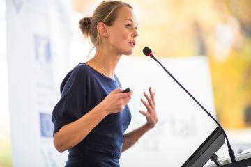 A self-assured woman stands at a podium addressing an audience