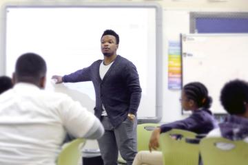 A young man stands at a white board, teaching a middle school class