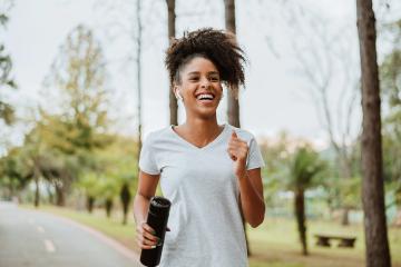 A happy woman is running on a roadside and carrying a water bottle