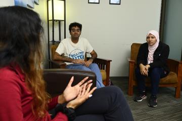 A student, facing away from the camera, talks to two other students in the A Place to Talk room